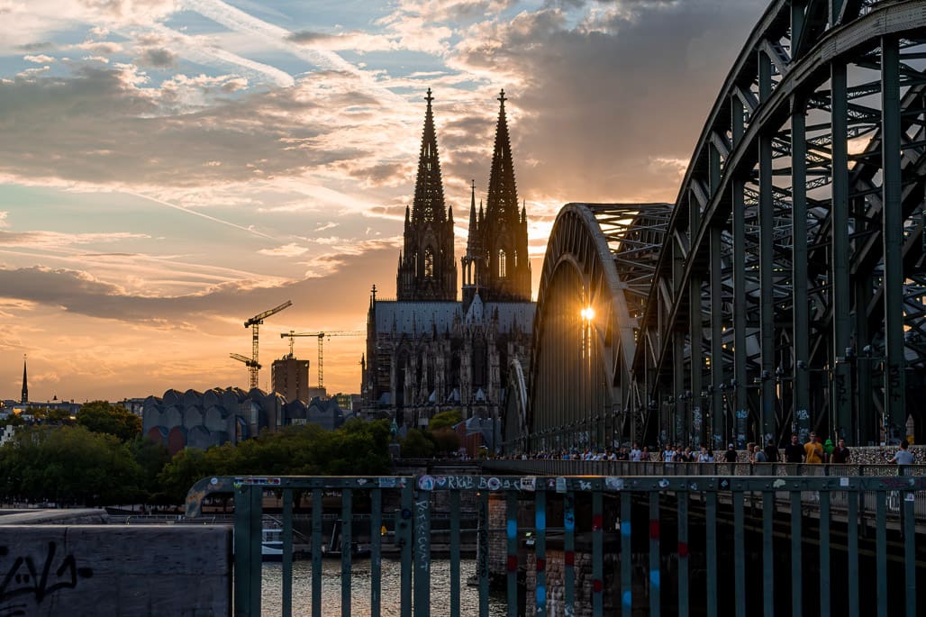 Kunstfotografie Köln porträtiert Hohenzollernbrücke und Dom vor dramatisch getönter Abendsonne über Rhein.