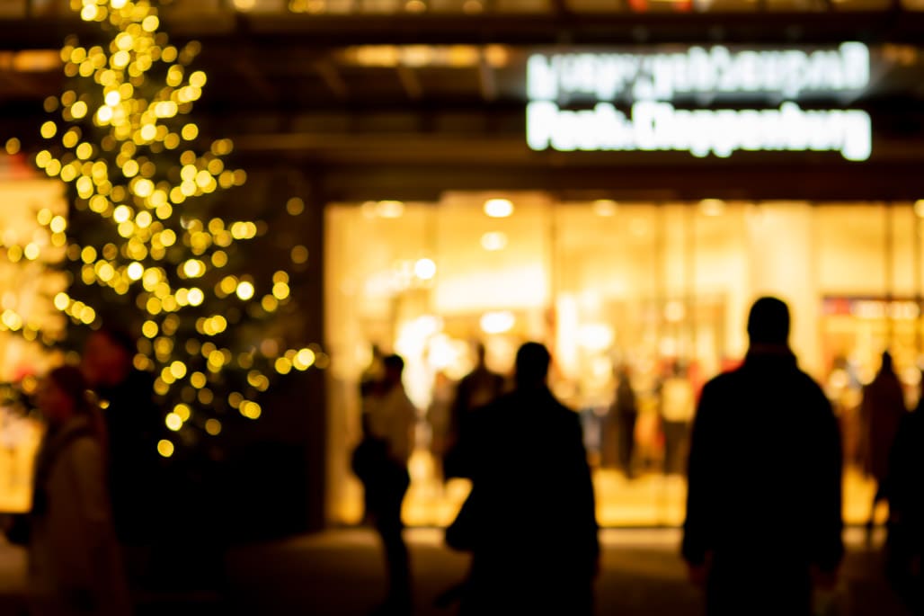 Kunstfotografie Köln zeigt unscharfe Silhouetten vor leuchtendem Weihnachtsbaum im Kaufhaus-Eingang.