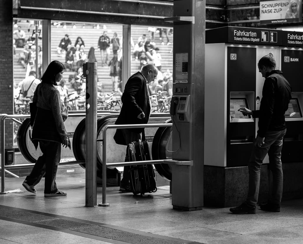 Streetphotography zeigt Reisende am Kölner Ticketautomaten vor Metrozugang, alltäglicher Pendlerblick.