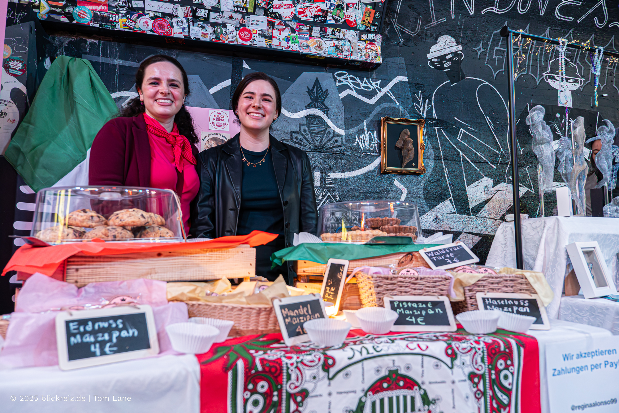 Stand mit zwei Ausstellerinnen auf der Hormiga Brava Messe Köln, präsentiert werden Marzipanvarianten und Gebäck aus lateinamerikanischer Tradition.