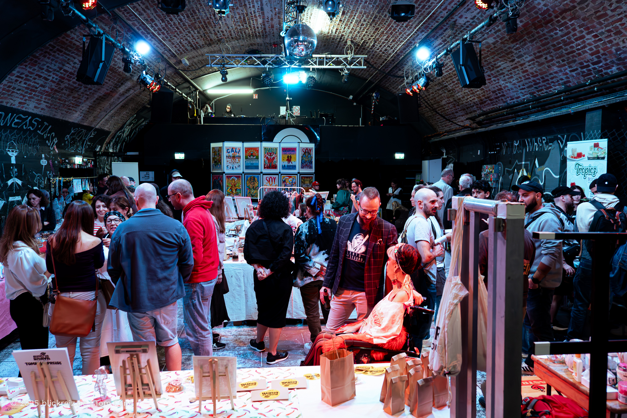 Menschenmenge auf der Hormiga Brava Messe Köln, lebendige Stimmung unter Backstein-Gewölben mit Kunst- und Modeständen.