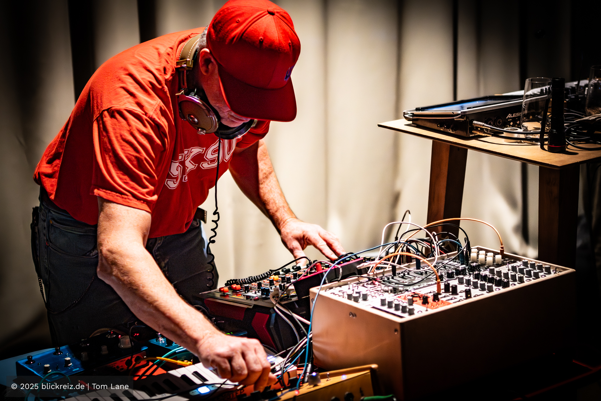 Endo Monk arbeitet an modularen Synths und Effektgeräten, warmes Licht akzentuiert Kabel, Regler und Bewegung.